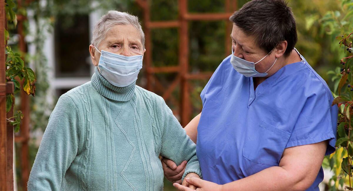 A care worker walking with an elderly woman through the garden.