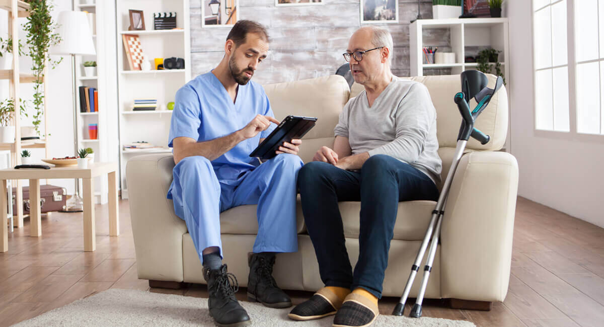 A male care worker assisting an elderly disabled man in sorting bills.