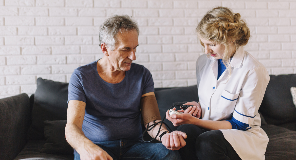 A agency carer checks an seniors BP while providing homecare service