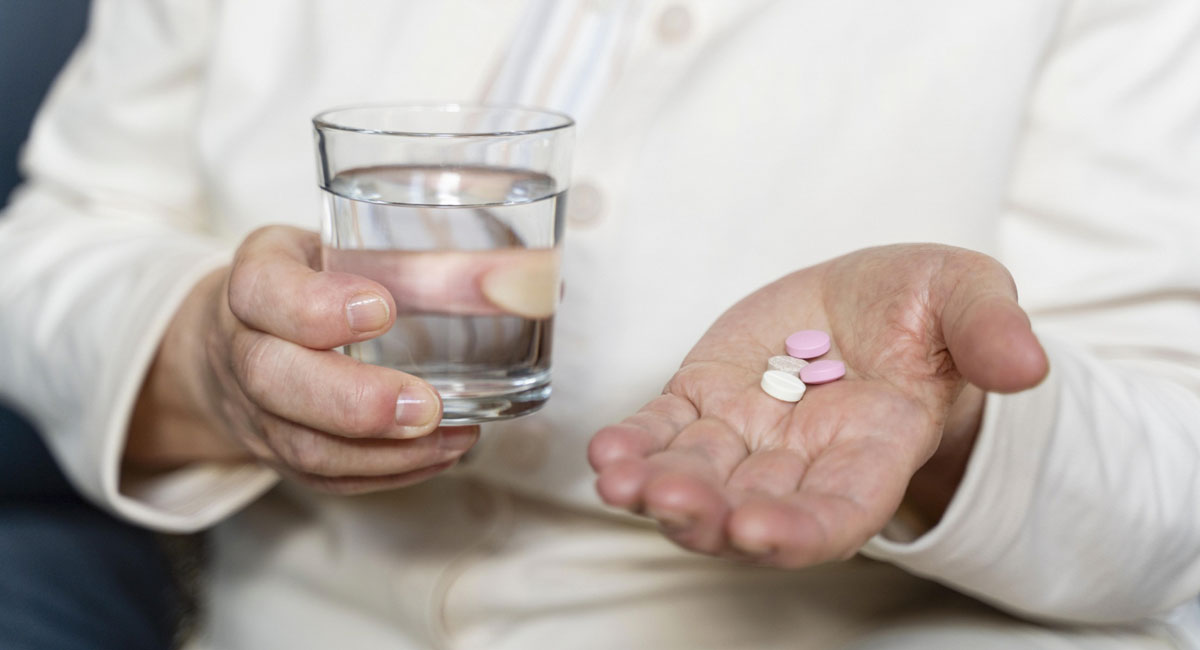 The hands of a patient taking medicines and a glass of water