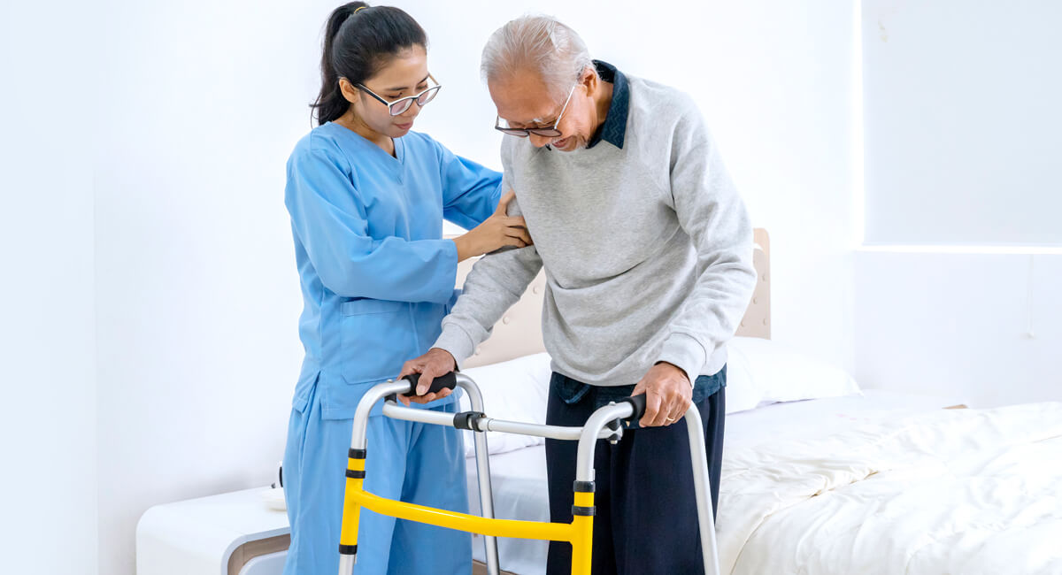 A live-in carer assists an elderly woman in walking down the corridor