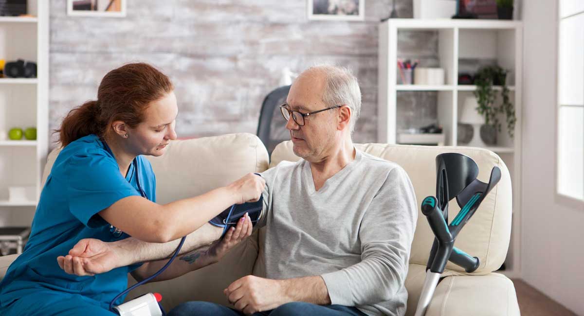 A female carer checking the blood pressure of a senior man.