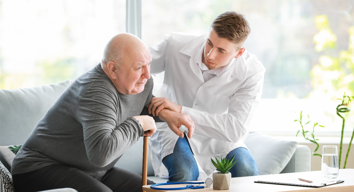 A carer assists a disabled elderly person in getting up from the sofa.