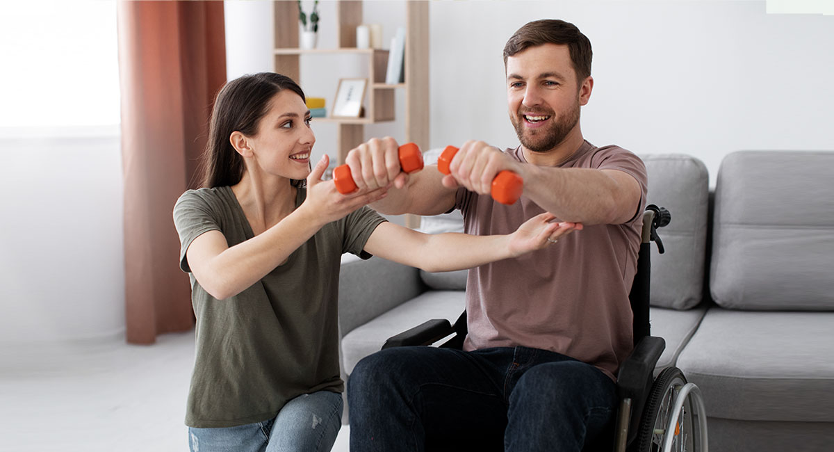 A carer guiding a physically disabled person to exercise at home.