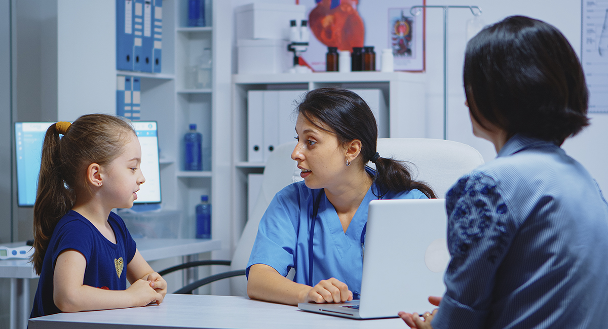 A nursing staff member converses with a girl child while diagnosing