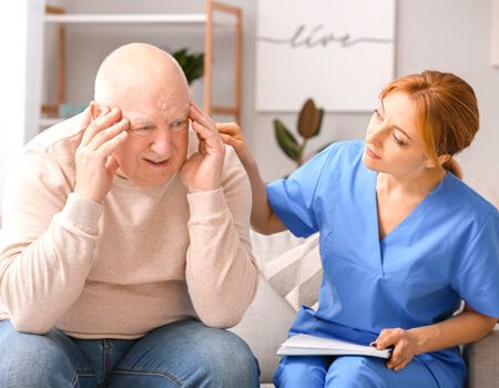 A caregiver assists an elderly person who is suffering from a headache