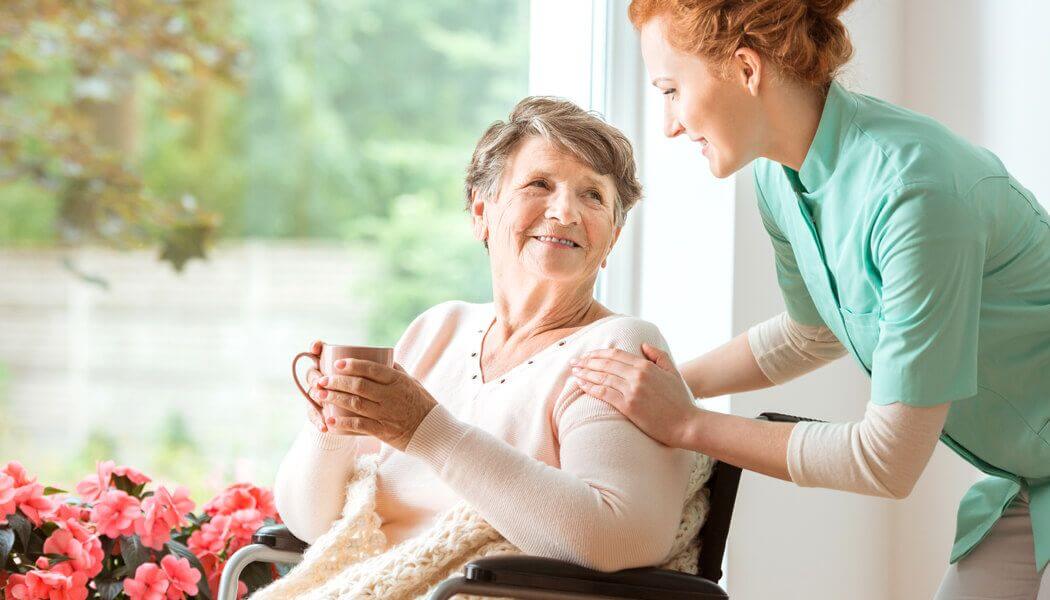 A caregiver offers emotional support to an elderly person in a wheelchair