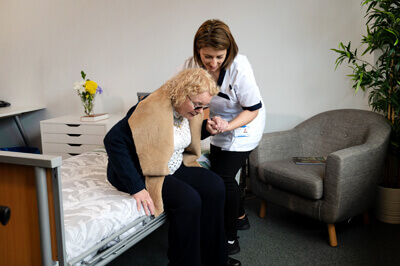 A live-in care worker encouraging an elderly woman to get out of bed